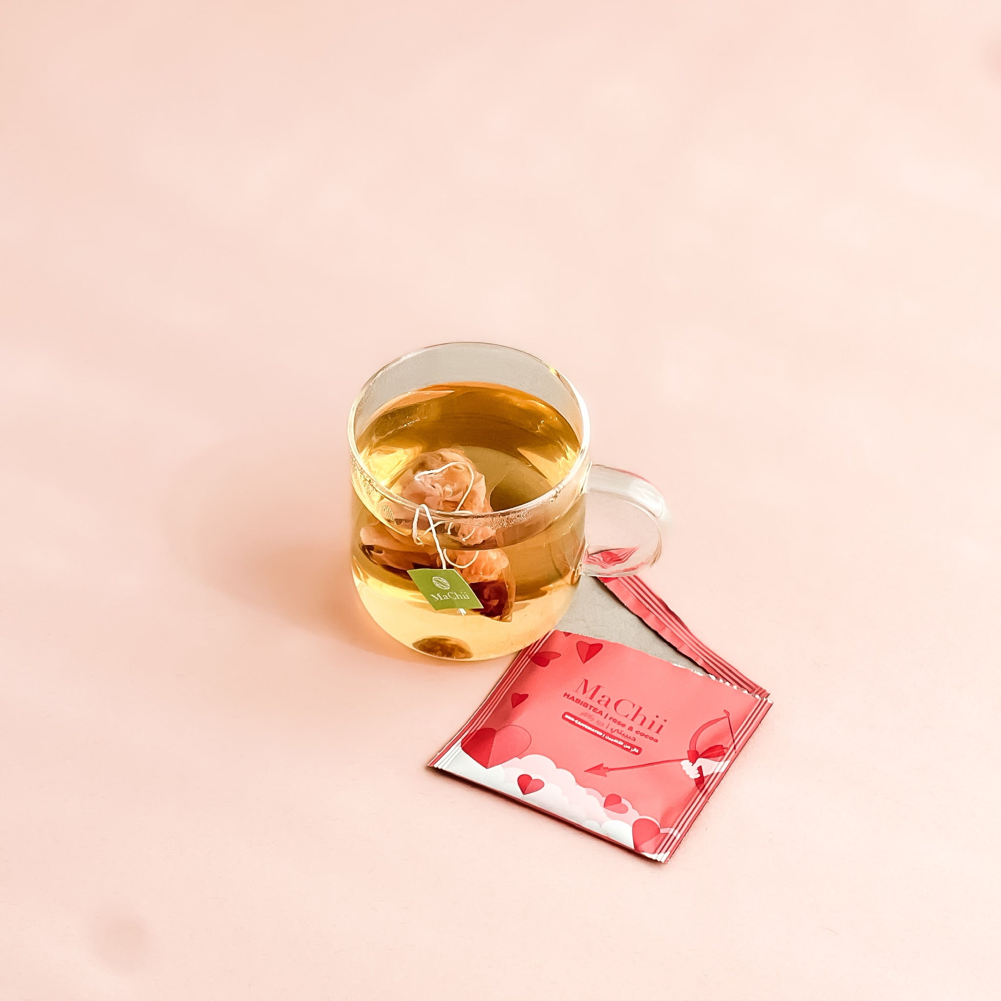 organic silk tea bag brewing in a glass mug. the tea is made of rose and cocoa tea.