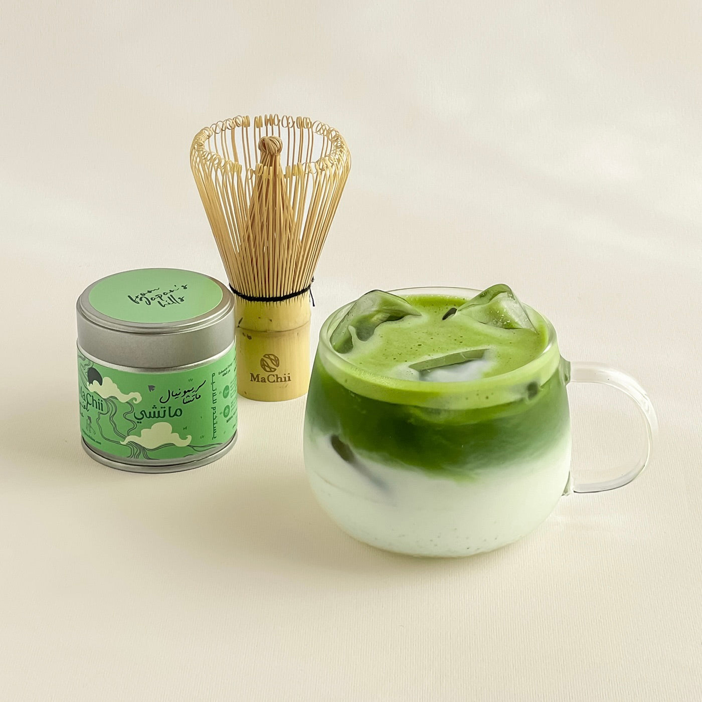 A cup of matcha green tea with a whisk next to it. A MaChii Tea tin on the side.