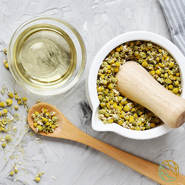 organic loose leaf chamomile tea spread out across the table. chamomile tea brewing in a cup next to the leaves